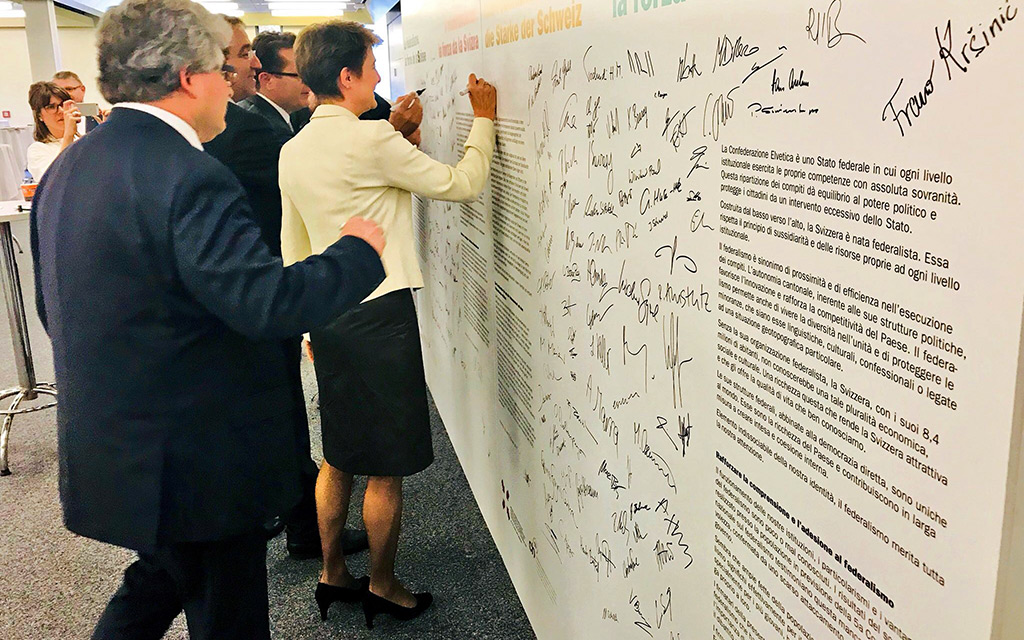 La conseillère fédérale Simonetta Sommaruga se tient debout devant un mur et signe la Déclaration de Montreux qui y est imprimée